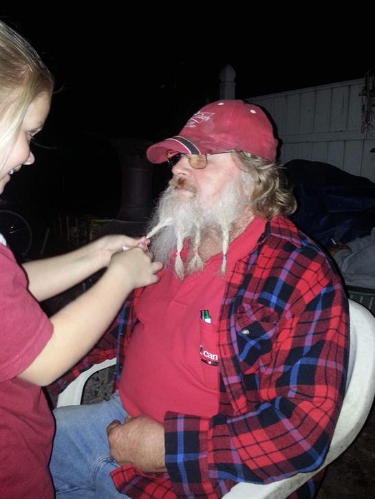 A young girl trims the beard of a man sitting in a chair, enjoying a fun moment together.