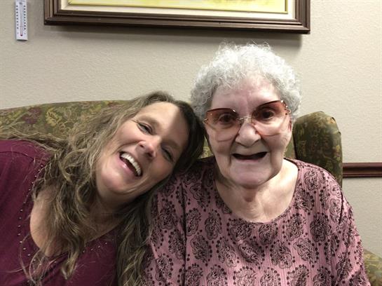 A woman and her grandmother share a happy moment while sitting together on a couch.