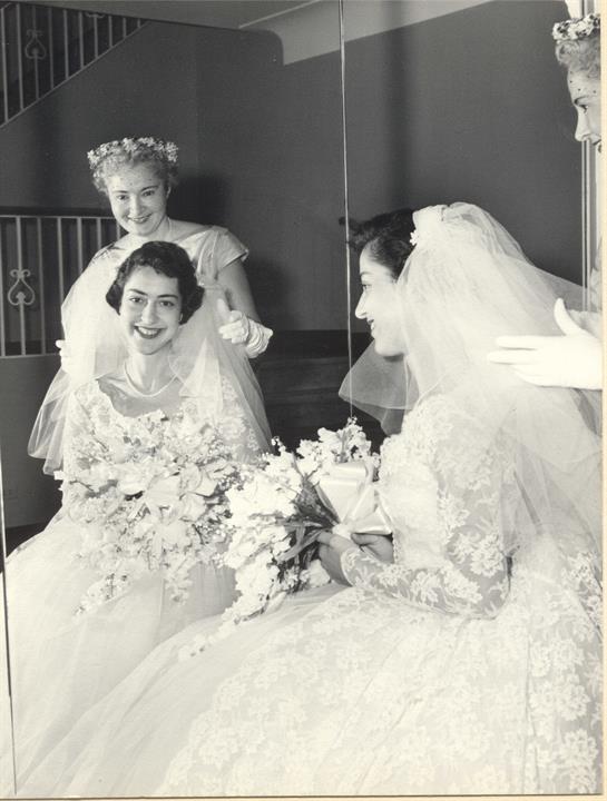 Bridesmaids help the bride prepare and share smiles in a vintage setting before the ceremony.