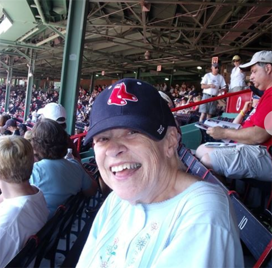 A cheerful woman smiles while watching a baseball game, surrounded by excited fans in a stadium.