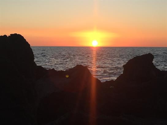 Sunset casts vibrant colors over the ocean while standing on rocky coastline by the sea.
