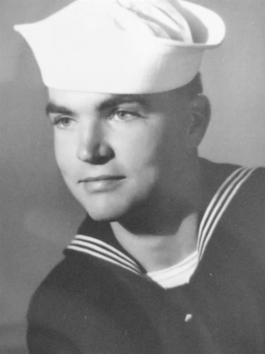 A young sailor in uniform wearing a cap gazes confidently at the camera with pride.