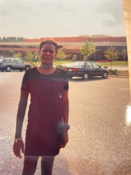 A woman poses in a parking lot, showcasing her outfit while cars are parked nearby.