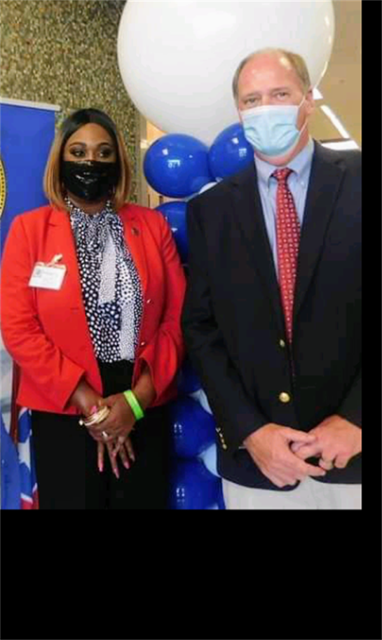 Two community leaders pose at a lively event with balloons and colorful decor, engaging attendees.