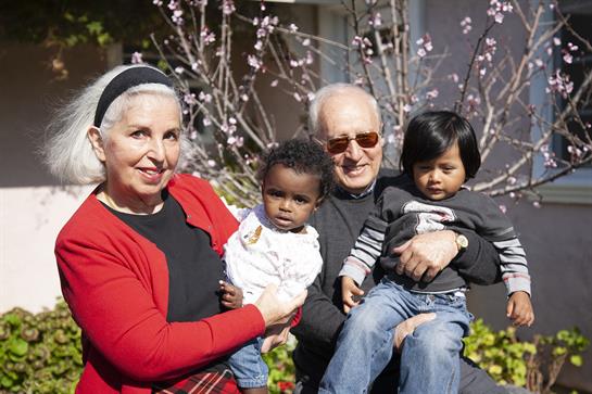 Grandparents joyfully hold their grandchildren in a vibrant garden filled with blooming flowers.