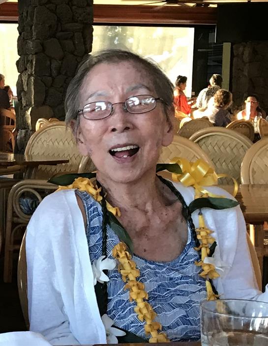 Elderly woman with glasses laughs joyfully while surrounded by cheerful diners at a celebration.