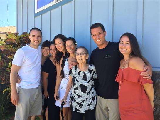 A joyful family stands together outside a blue building, sharing happy moments in summer.