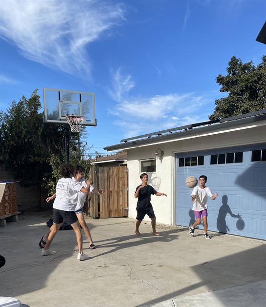 Four children engage in a lively basketball game in a spacious backyard under sunny weather.