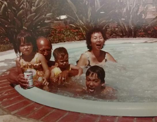 A joyful family gathers in a backyard pool as children splash and play with smiles and laughter.