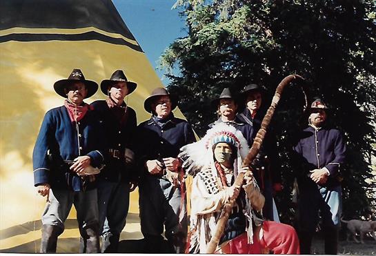 Historical figures in traditional costumes gather outside a colorful tent, sharing culture.