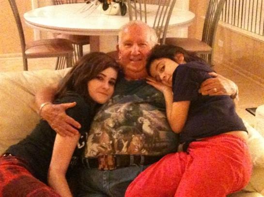 Two young women relax and enjoy a close moment with an older man while sitting on a couch.