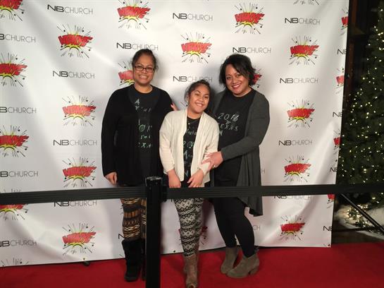 Three women and a girl smile warmly in front of a decorated backdrop.