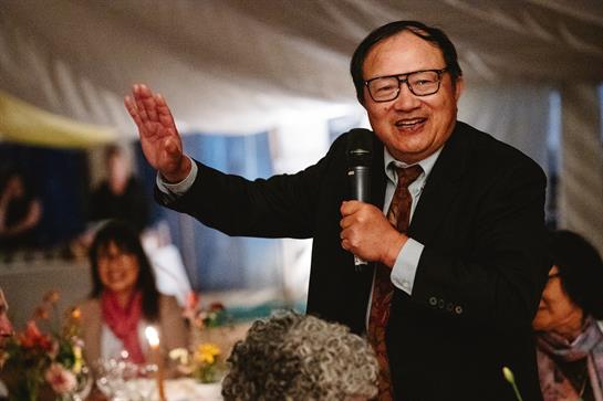 A man gestures and laughs while engaging with attendees at a festive event.