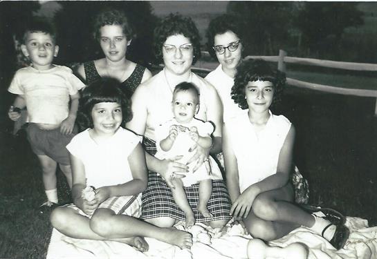 A group of six girls and a baby are seated together outdoors, showcasing laughter and joy.