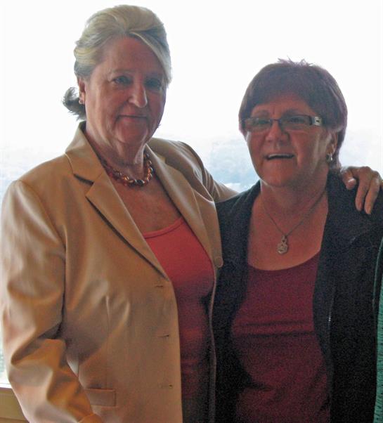 Two women stand side by side, enjoying a joyful moment in a sunlit high-rise location.