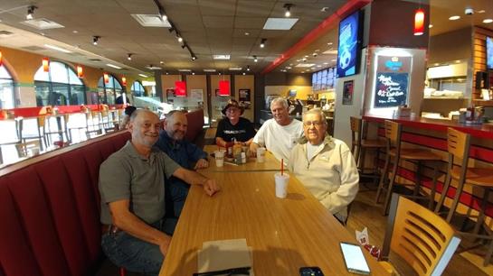 Five friends converse and share laughs around a wooden table in a busy restaurant setting.