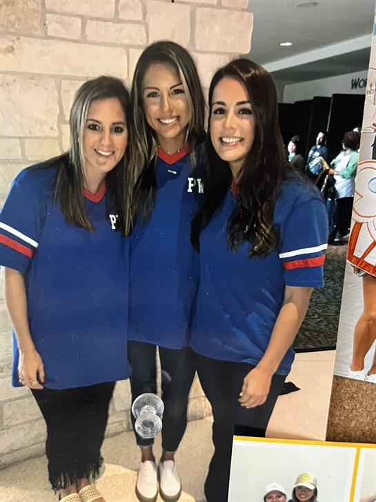 Three friends stand together in blue shirts, enjoying an event filled with excitement and energy.