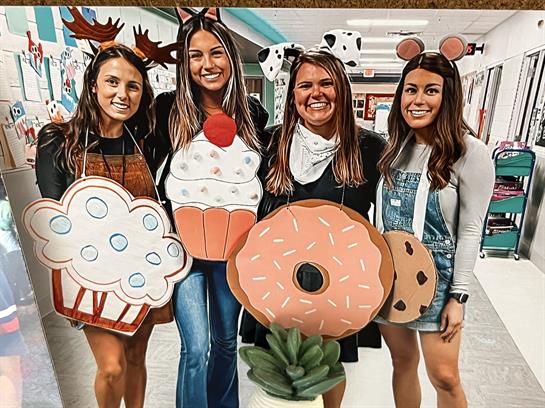 Friends join together wearing large, playful food-themed costumes in a lively school setting.