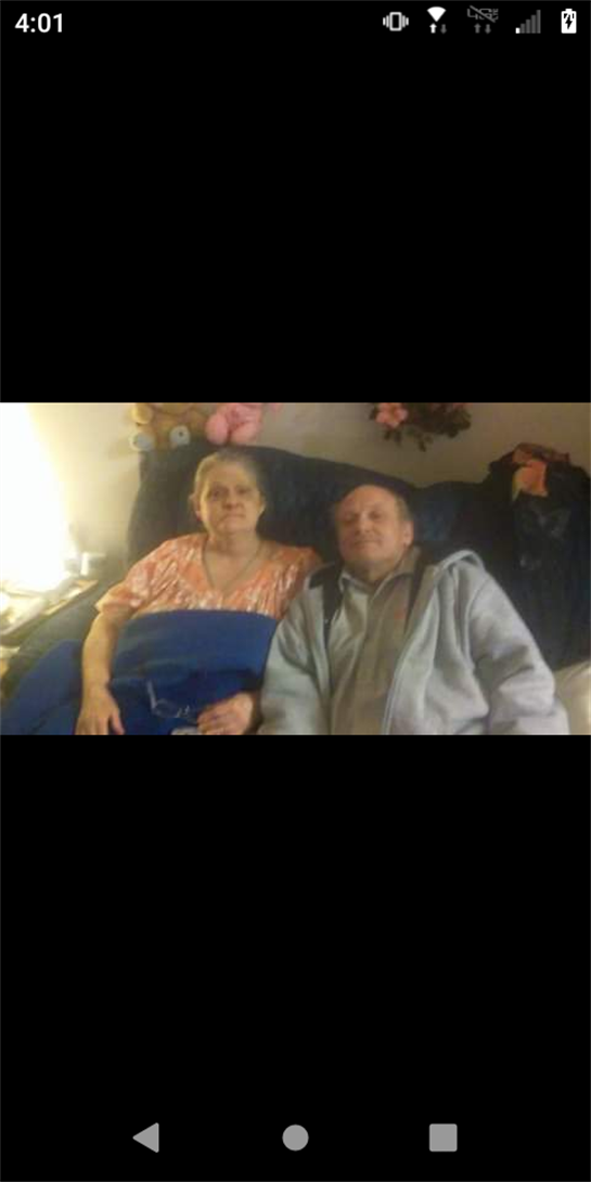 An elderly couple shares a warm moment on their bed in a cozy room decorated with personal touches.