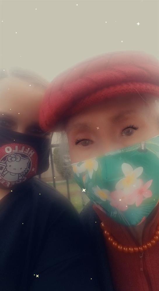 Two women with colorful masks share a joyful moment outside in the park under the sun.