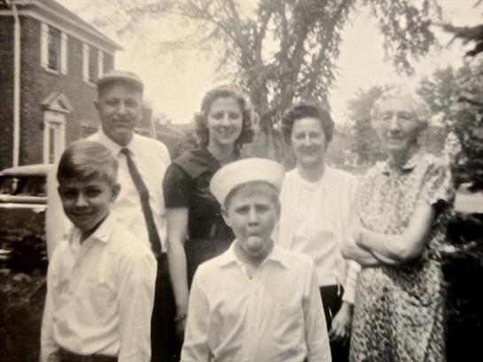 Six people smile together in a nostalgic outdoor setting, showing their camaraderie.