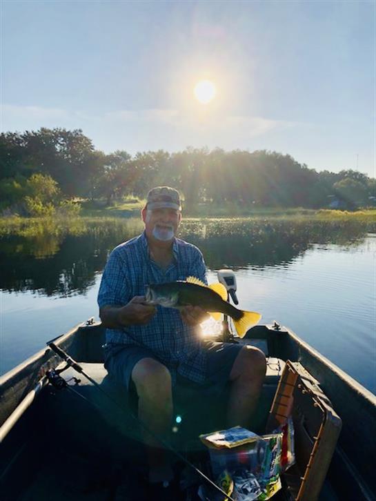 A man sits in a small boat, catching fish in tranquil waters at dawn.