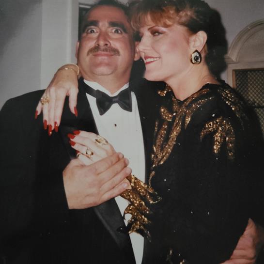 Elegantly dressed individuals embrace and smile warmly at a glamorous gathering.