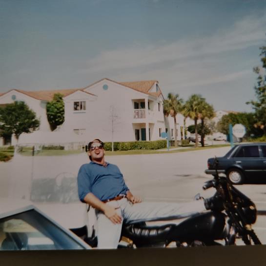A man enjoys his leisure time on a motorcycle near apartment buildings in bright weather.