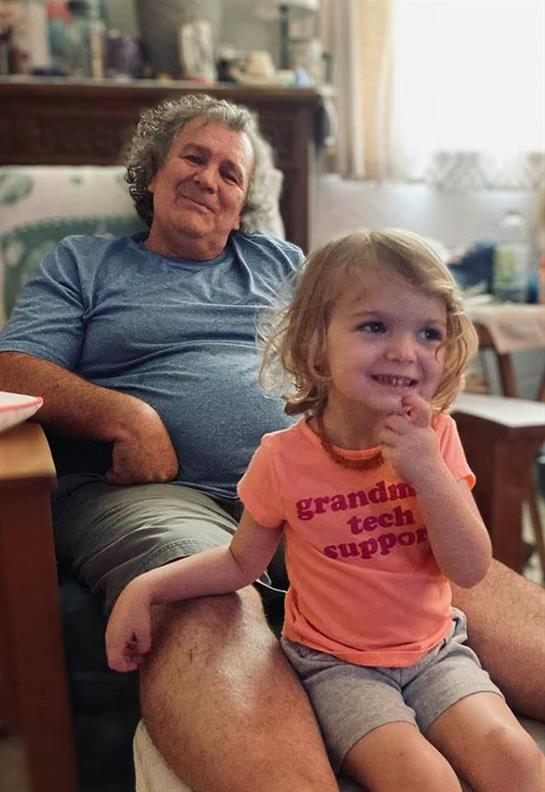 A grandmother enjoys time with her granddaughter, who is playfully smiling in a relaxed setting.