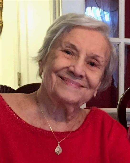 Elderly woman wearing red smiles warmly while seated at a table surrounded by friends.