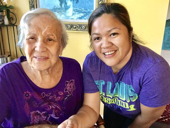 An elderly woman smiles next to a younger woman, sharing a warm moment together.