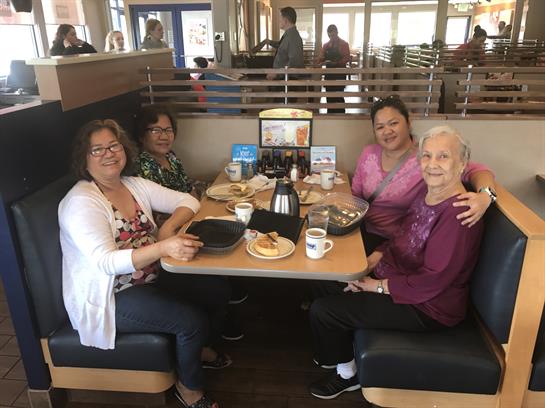 Four friends share laughter and breakfast in a lively restaurant setting with warm ambiance.