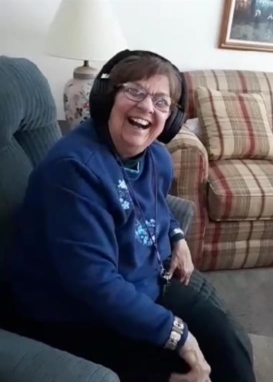 Woman in headphones smiles while relaxing in a cozy chair with holiday decor.