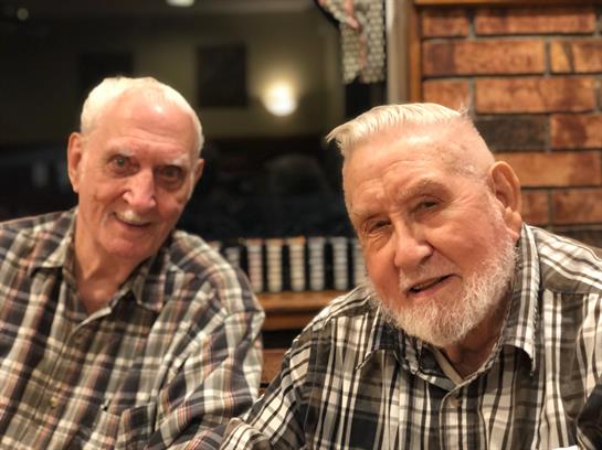 Two older men in matching plaid shirts smile joyfully as they enjoy their time together.
