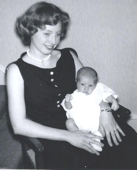 A smiling woman in a black dress holds a baby, creating a heartwarming scene of connection and joy.