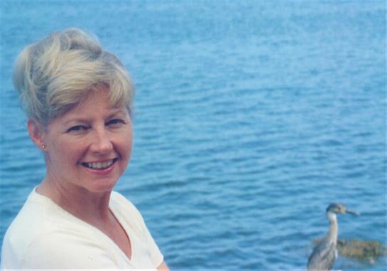 A woman smiles on a sunny day by the ocean, with beautiful blue water behind her.
