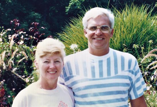 Joyful elderly couple poses in vibrant garden, enjoying a warm day filled with greenery.