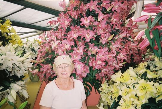 A woman happily poses beside a tall display of pink lilies at a spring flower show.