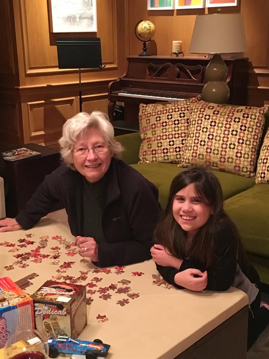 A grandmother and granddaughter solve a puzzle together in their cozy living room.
