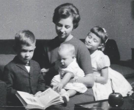 Mother holds her baby while reading to two other children in a comfortable setting.
