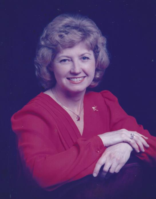 A woman with curly hair smiles brightly while posing confidently in a red dress.