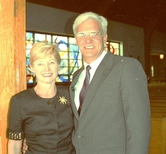 Two individuals smile warmly while standing side by side in a beautifully lit setting.