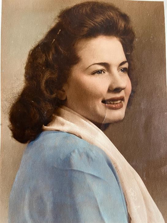 A young woman with curly hair gazes to the side, wearing a light blue dress and a soft scarf.