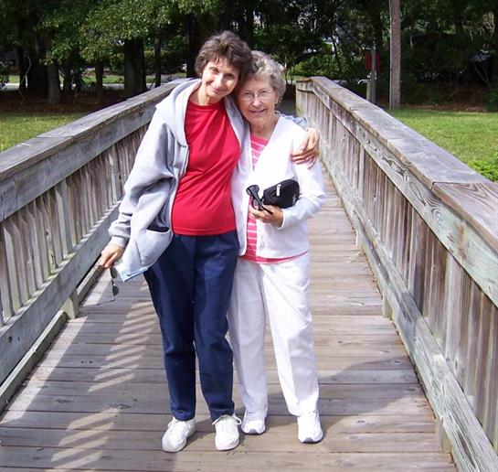 Two women enjoying each other's company while posing on a bridge in a park.