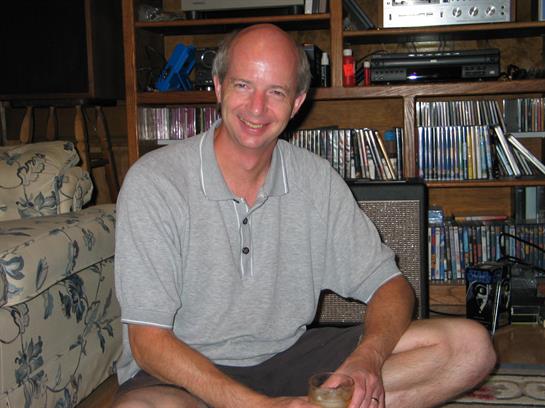 Relaxed man smiles while sitting on the floor with a drink in a warm, inviting living room.