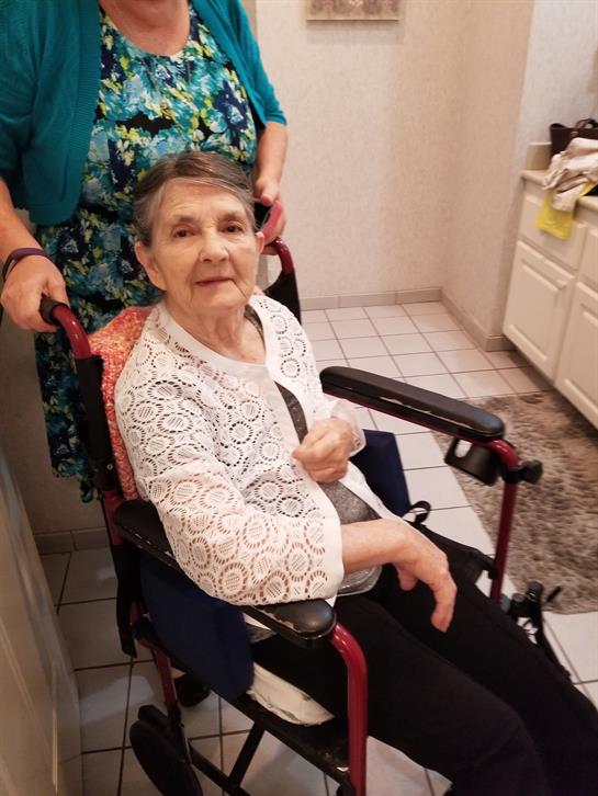 Caregiver assists older woman in wheelchair at home as they share a moment together.