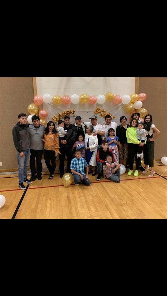 A diverse group of family members celebrates an event with colorful balloons in a gymnasium.