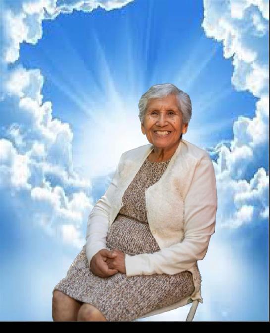 Elderly woman with gray hair sits happily in front of a sunny sky surrounded by clouds.