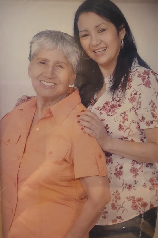 Two women, a mother and her daughter, smile brightly while standing close together.