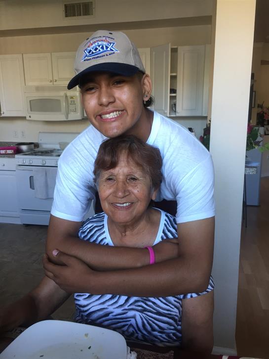 A young man embraces his smiling grandmother in a cheerful kitchen full of light.